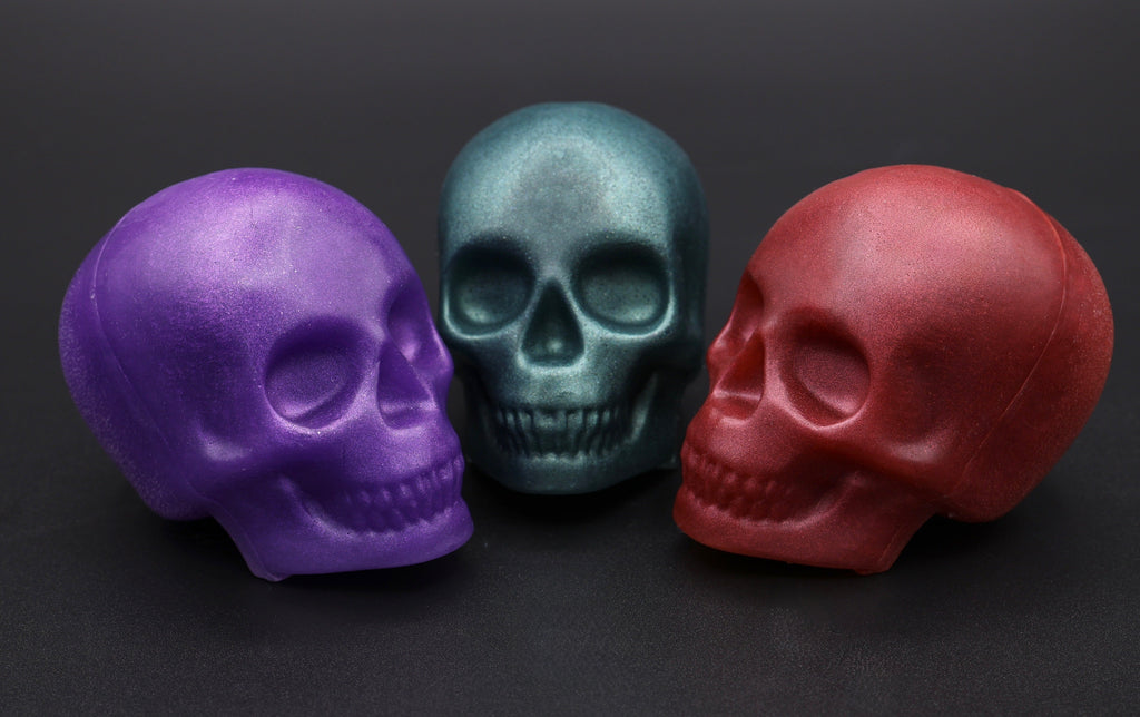 Three skull soaps in purple, teal and red shown from a side angle