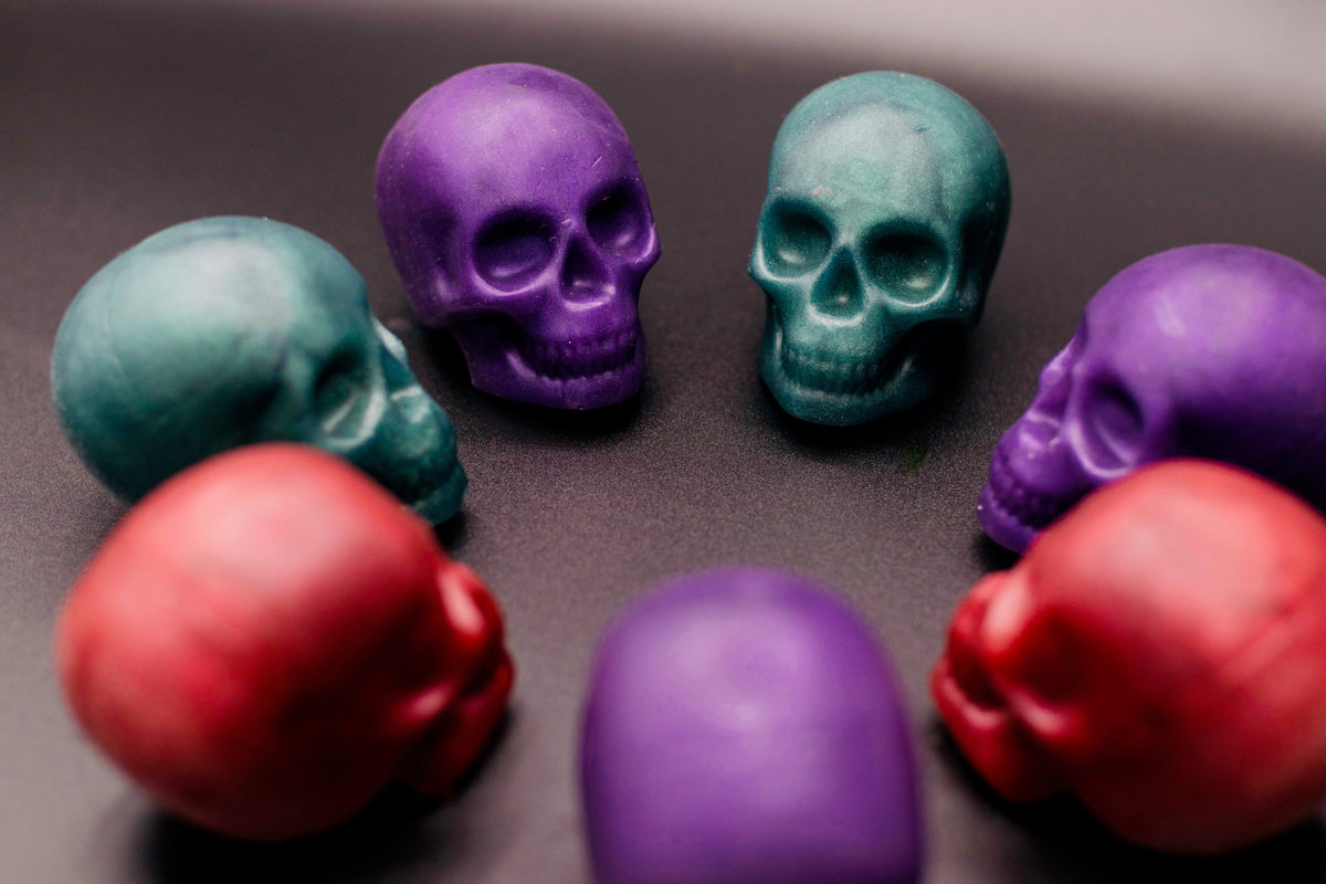 Multiple skull soaps scattered on a dark surface showing all three colors